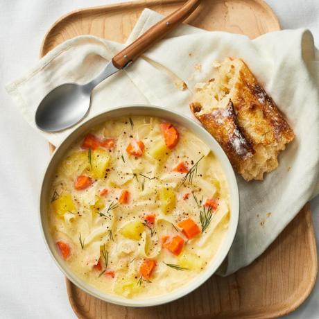 Una ciotola di zuppa cremosa di patate e cavolo cappuccio accanto a un cucchiaio e un pezzo di pane tostato